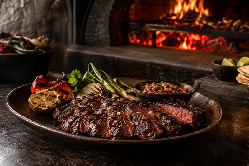 Corte a la parrilla con vegetales y salsa frente al horno de carbón
